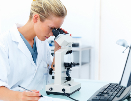 Young female researcher looking into a microscope and writing notes at laboratory